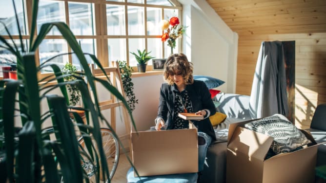 Junge Frau zieht während der Coronakrise in einen neue Wohnung um und packt Kisten aus