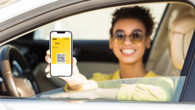 Frau zeigt aus dem Fenster ihres stehenden Autos die ADAC Mitgliedskarte auf ihrem Smartphone - ADAC Mitgliedskarte