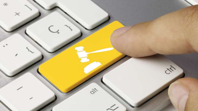 Mann drückt auf Tastatur mit Richter Hammer - Online-Assistenten ADAC Rechtsschutz