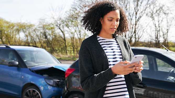 Frau meldet Kfz Schaden über Smartphone, im Hintergrund ein Auffahrunfall - Schadenmeldung Kfz ADAC