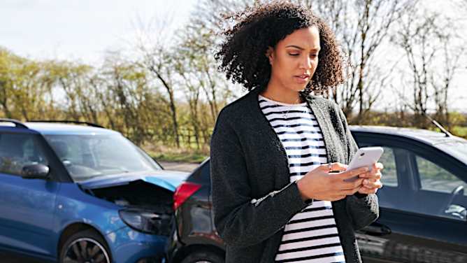 Frau meldet Kfz Schaden über Smartphone, im Hintergrund ein Auffahrunfall - Schadenmeldung Kfz ADAC