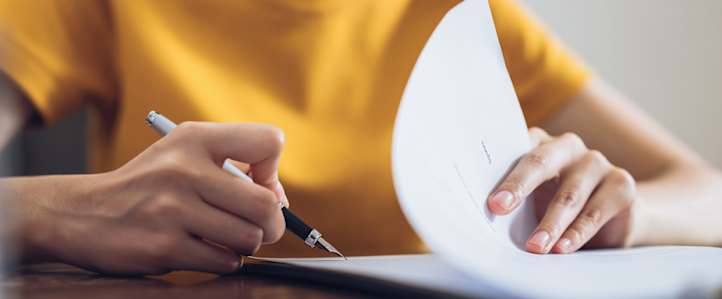Close Up einer Frau im gelben T Shirt, die einen Vertrag unterzeichnet