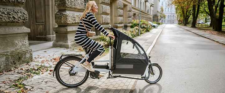 E Bike Versicherung: Frau auf E-Lastenrad in der Stadt unterwegs