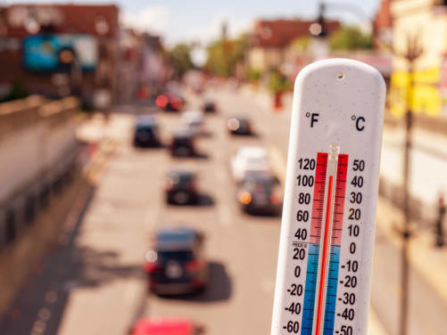 Hitze - ein Thermometer zeigt 40 Grad im Close Up im Hintergrund eine befahrene Stadtstrasse im Sommer