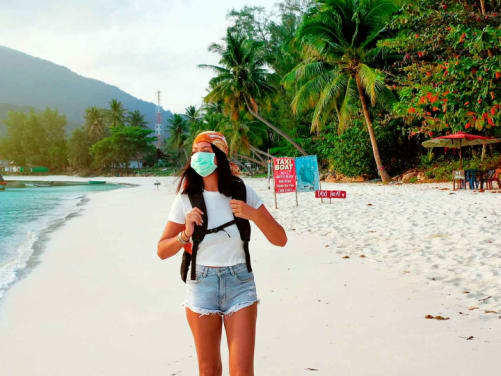 Reiseversicherung: Frau im Urlaub am Strand währen Corona