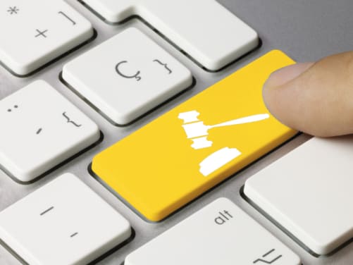 Mann drückt auf Tastatur mit Richter Hammer - Online-Assistenten ADAC Rechtsschutz