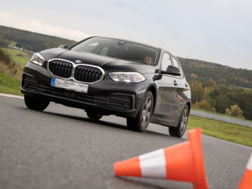 Frau steuert schwarzen BMW durch einen Slalomparcour