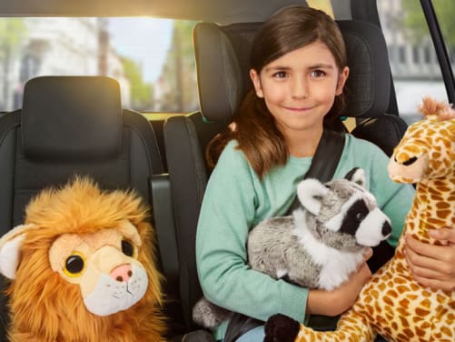 Maedchen sitzt mit Plüschtieren im Auto - Autoversicherung ADAC