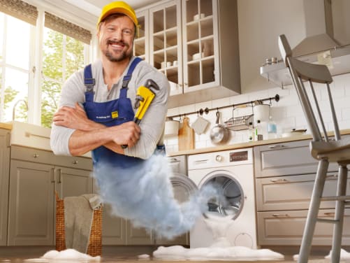 Handwerker mit Rohrzange erscheint aus Waschmaschine - ADAC Zuhause-Schutzbrief