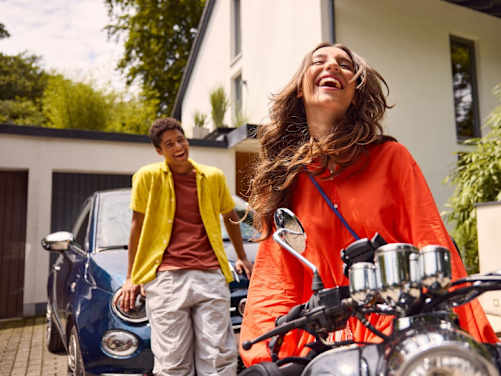 Zwei junge Leute lachend mit Roller und Auto