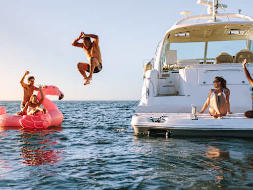 Haftpflicht im Ausland: Freunde auf Boot im Meer, Mann springt in das Wasser