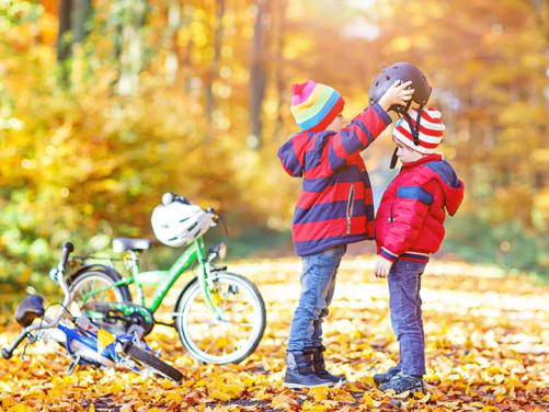 Kinder im Herbst mit dem Fahrrad setzen sich einen Helm auf