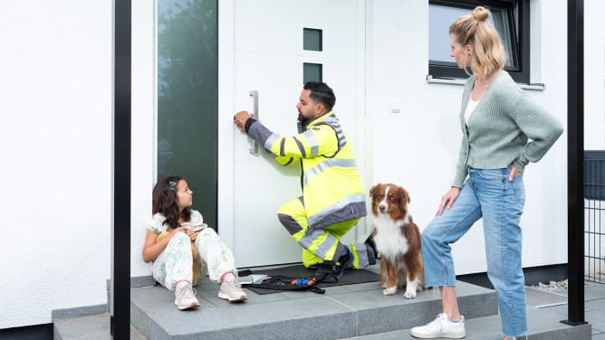 ADAC SChlüsselnotdienst helfer arbeitet an der Öffnung der Tür. Mutter, Tochter und ein Hund warten davor.
