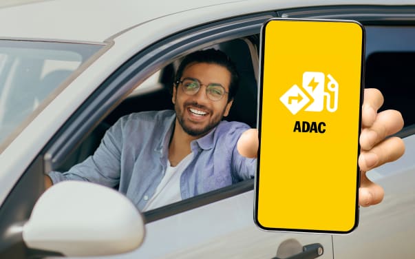Ein Mann sitzt im Auto und hält ein Handy in die Kamera. Auf dem Handydisplay ist das Logo der ADAC Drive App zu sehen.