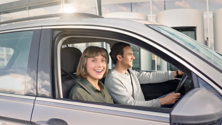Paar im Auto schaut lachend aus dem Fenster - Autoversicherung ADAC