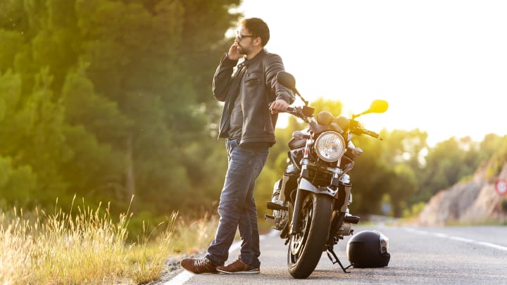 Mann telefoniert auf Stra�e neben Motorrad - ADAC Motorradversicherung