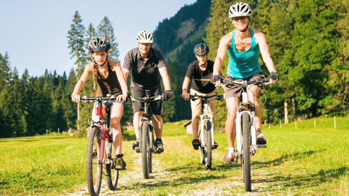 Familie fährt mit Mountainbikes über Wiese - Unfallversicherung ADAC