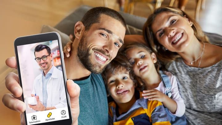 Familie auf der Couch, Mann hält Handy mit dem Screen der App in die Kamera