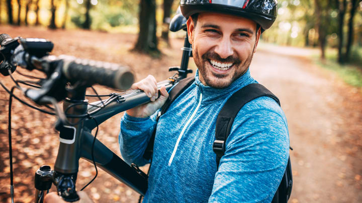 Mann schultert Mountainbike im herbstlichen Wald - Unfallversicherung ADAC