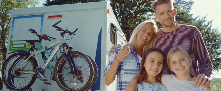 Vater, Mutter und zwei Töchter lächeln vor einem Wohnmobil
