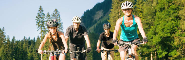 Familie fährt mit Mountainbikes über Wiese - Unfallversicherung ADAC