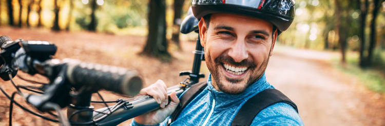 Mann schultert Mountainbike im herbstlichen Wald - Unfallversicherung ADAC