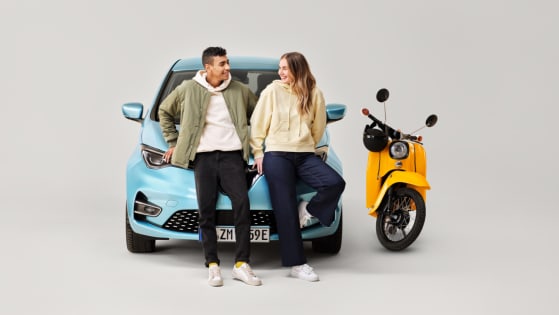 Zwei junge Leute lehnen an einem Pkw und ein Moped steht daneben