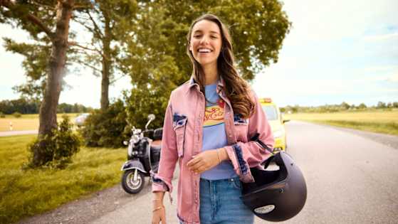 Junge Frau lächelt mit ihrem Rollerhelm am Arm