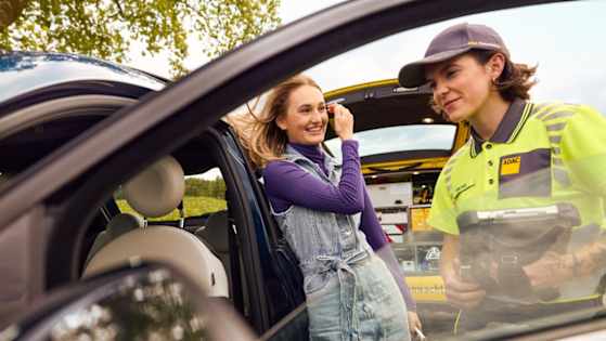 Junge Frau steht an ihrem Auto, das eine Panne hat und der ADAC hilft