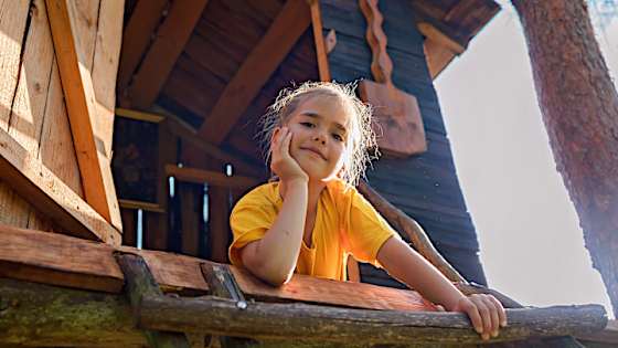 Mädchen liegt stolz und lächelnd vor ihrem Baumhaus - Wohnrechtsschutz ADAC