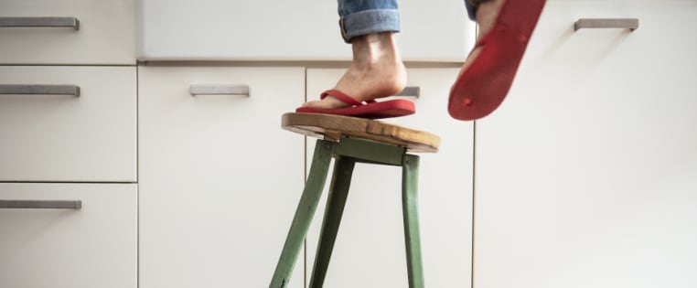 Frau steigt auf wackelnden Hocker, Haushaltsunfall - Unfallversicherung ADAC