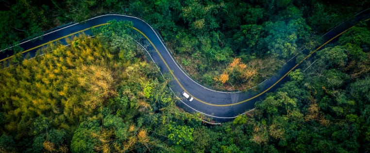 Auto fährt auf Straße durch grünen Wald - Ressourcenschonend Fahren ADAC