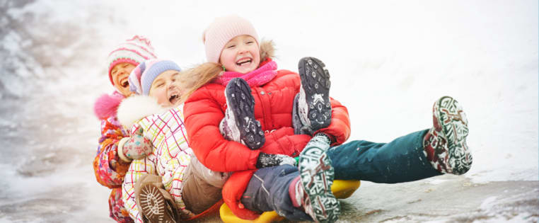 Kinder rodeln lachend den Berg hinunter - Unfallversicherung Kinder ADAC
