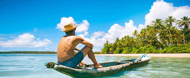 Mann sitzt in Longboat auf dem Meer und schaut auf einen Strand mit vielen Palmen