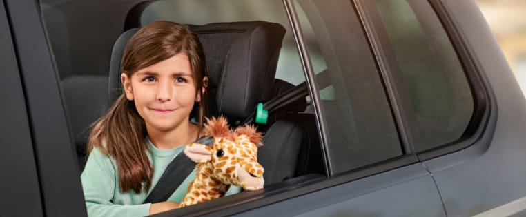 Maedchen schaut mit Plüsch-Giraffe aus dem Autofenster - Autoversicherung ADAC