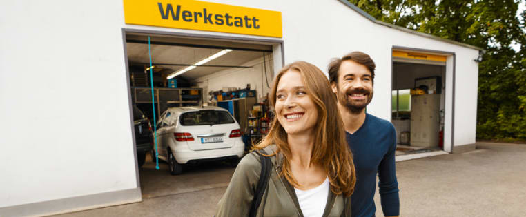 Lächelndes Paar bei einer Autowerkstatt