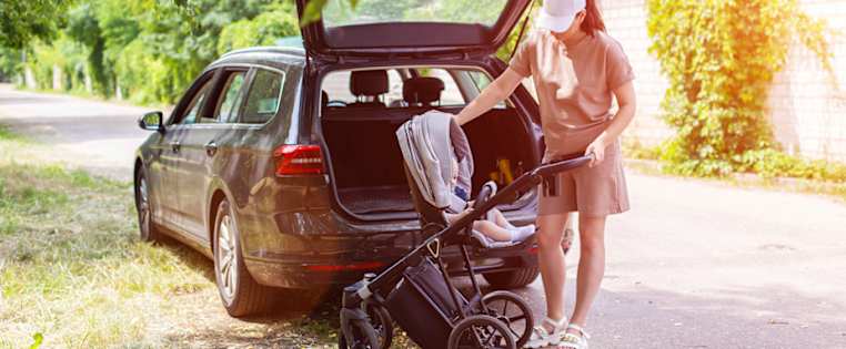 Junge Mutter steht vor Auto und klappt Babyschale vom KInderwagen - Kfz Versicherung Familienzuwachs