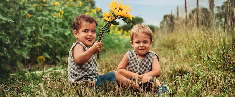 Zwei Jungen sitzen lachend vor Sonnenblumenfeld - Rechtsschutzversicherung ADAC