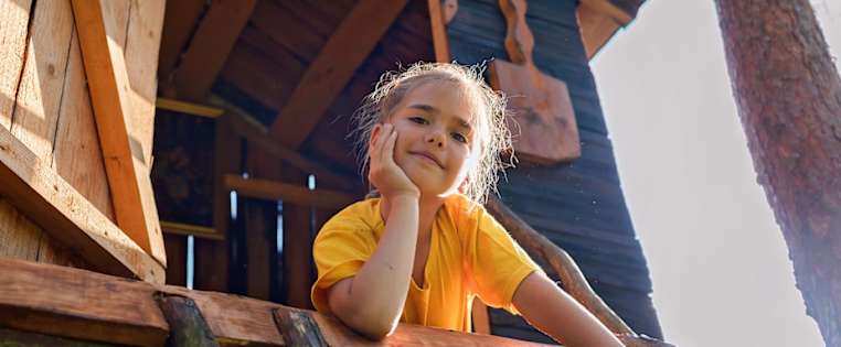 Mädchen liegt stolz und lächelnd vor ihrem Baumhaus - Wohnrechtsschutz ADAC