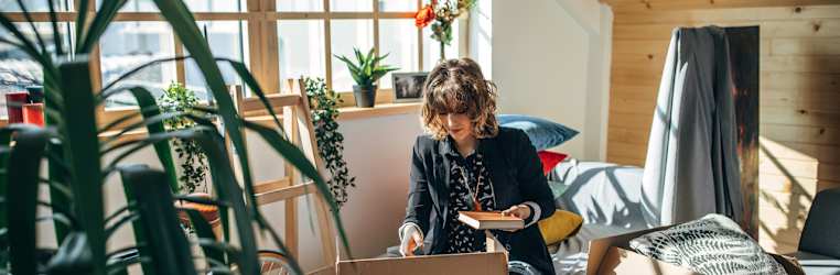 Junge Frau zieht während der Coronakrise in einen neue Wohnung um und packt Kisten aus