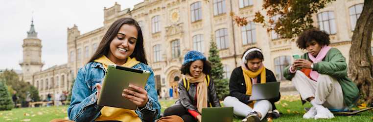 Vier Studenten sitzen vor einer alten Uni und schauen auf ihre Laptops