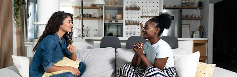 Zwei junge Frauen sitzen sich auf einem Sofa gegenüber und lächeln sich an