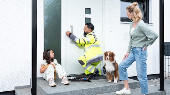 ADAC SChlüsselnotdienst helfer arbeitet an der Öffnung der Tür. Mutter, Tochter und ein Hund warten davor.