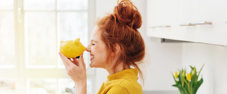 Junge Frau mit roten Haaren macht Nasenstüber mit einem gelben Sparschwein