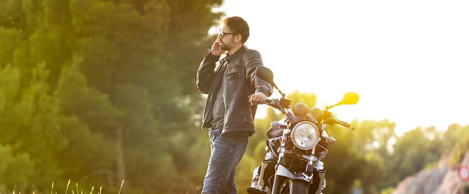 Mann telefoniert auf Straße neben Motorrad - ADAC Motorradversicherung
