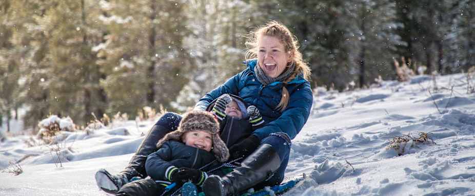 Mutte rund Kind fahren Schlitten - Auslandskrankenversicherung für Wintersportler ADAC
