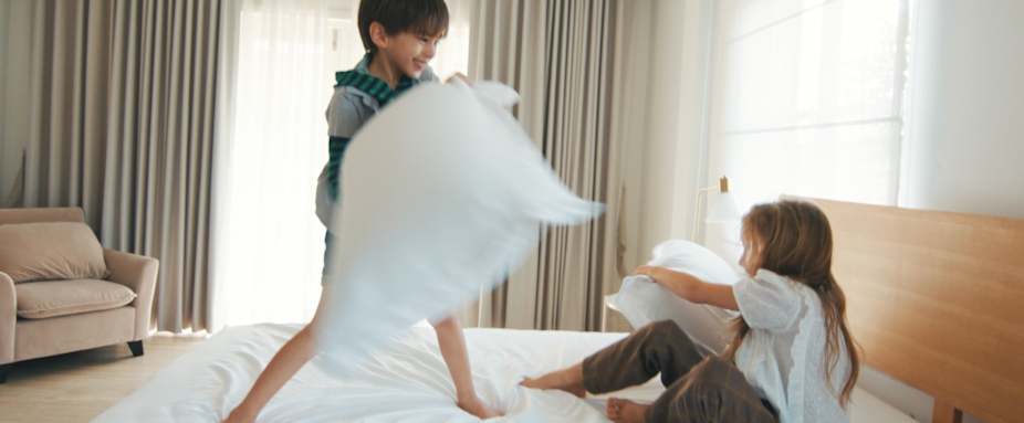Mädchen und Jung machen Kissenschlacht im Bett - private Rechtsschutzversicherung ADAC
