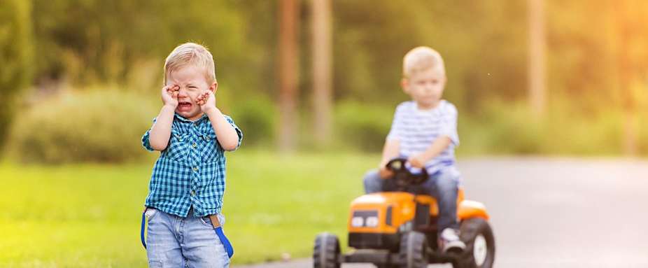 Ein Junge fährt auf Spielzeug-Traktor, ein Junge weint - Verkehrs-Rechtsschutz ADAC